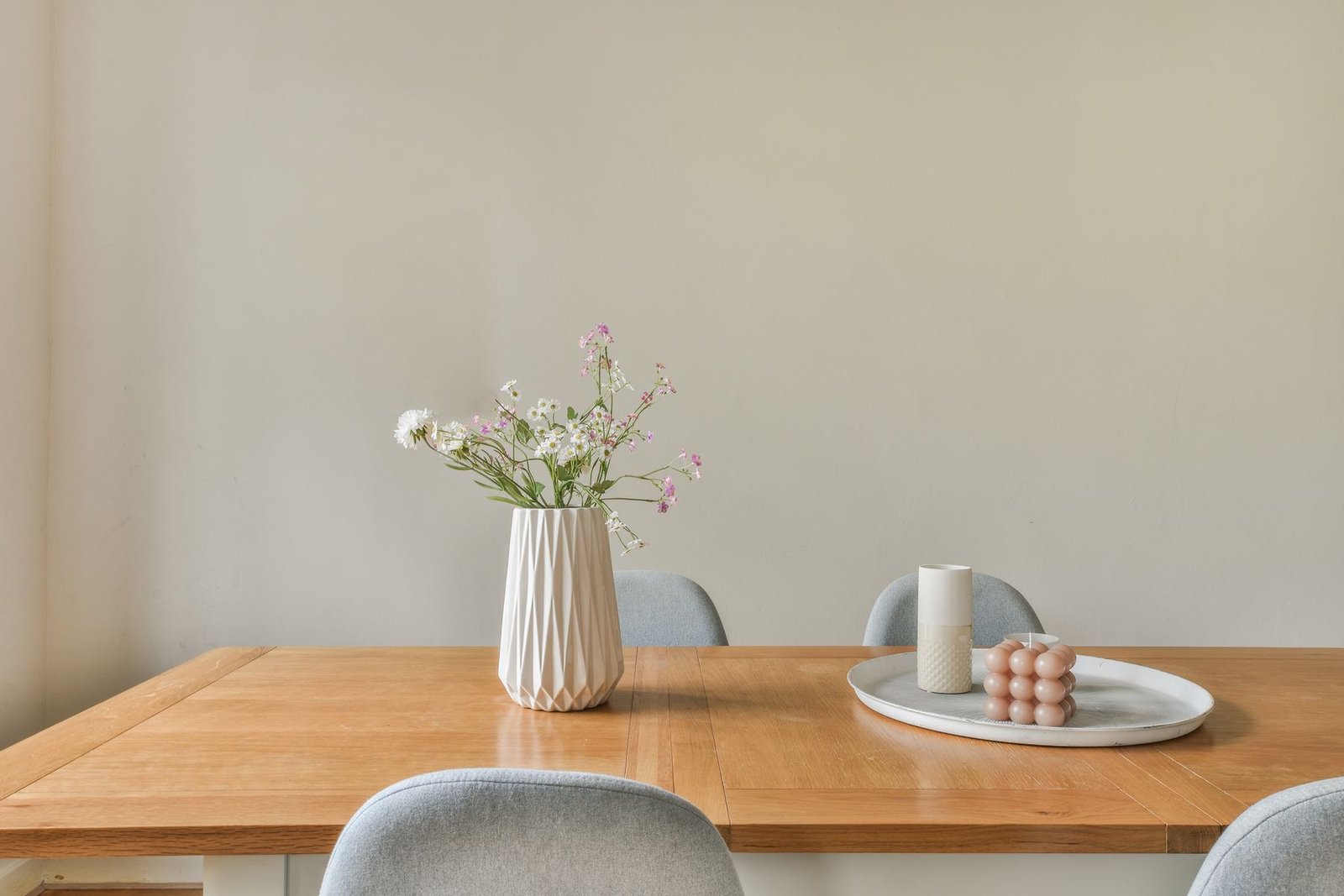 An oak table set with a white vase of flowers and candles